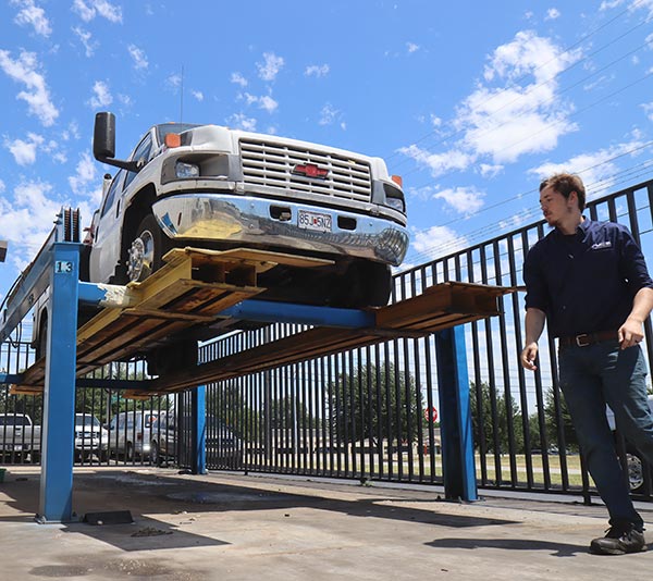 A transmission repair technician walks past a large commercial work truck on an outdoor lift.