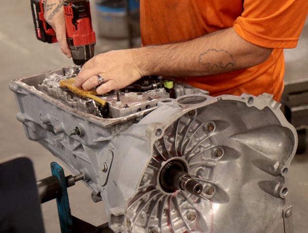 A man uses a power tool to build a remanufactured transmission in a factory.