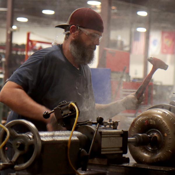 A man uses a mallet to build a remanufactured transmission in a factory.