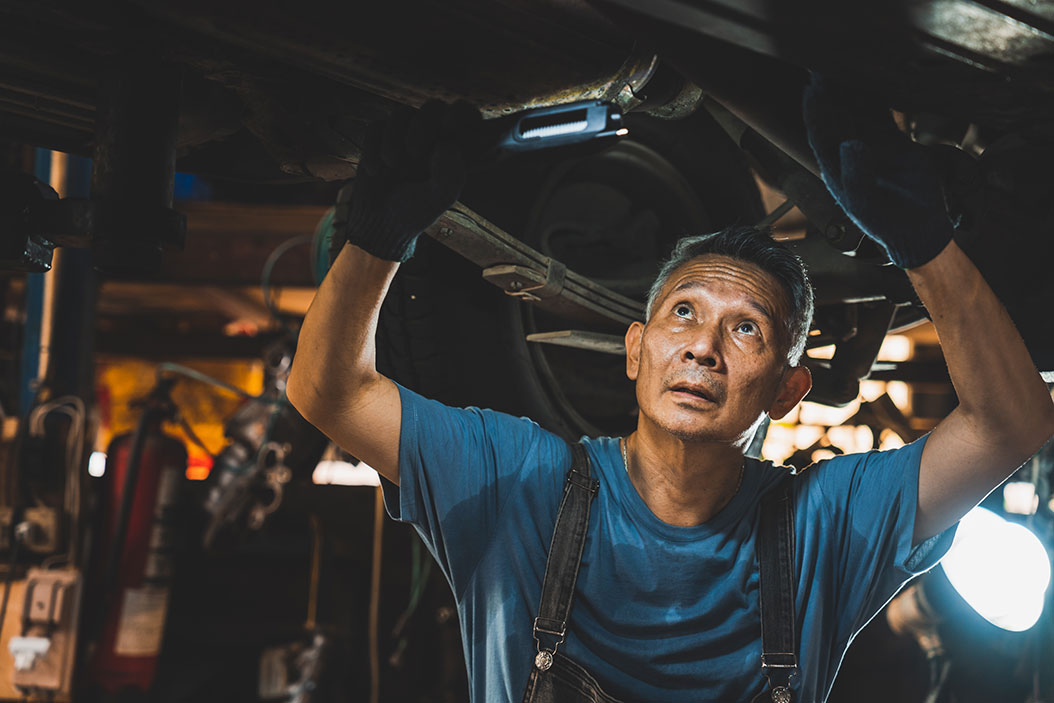 A technician examines under a vehicle near the transmission.