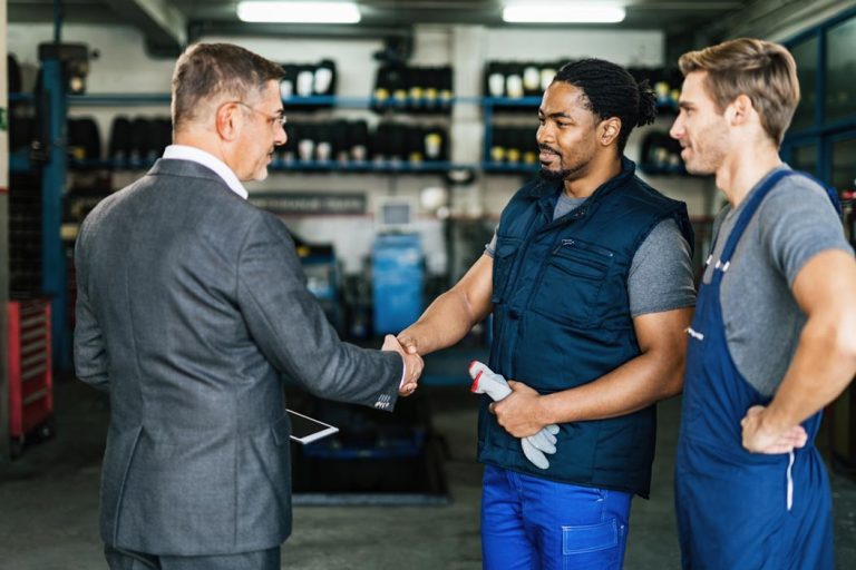 A mechanic and businessman meeting in an automotive repair shop.